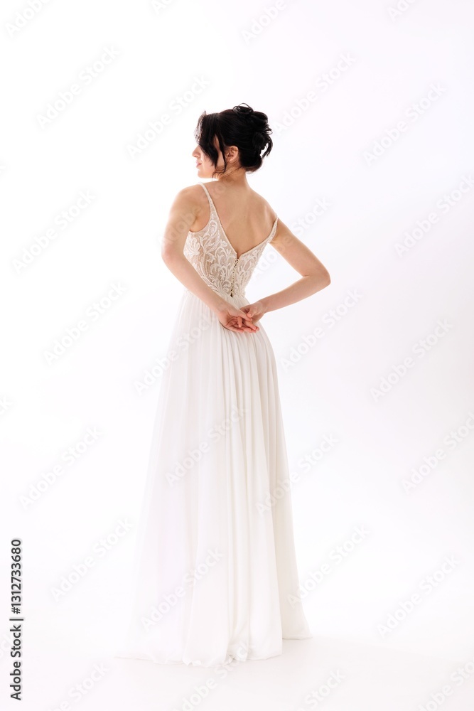 Elegant bride wearing a white wedding dress, facing away and holding her hands together in a serene studio setting