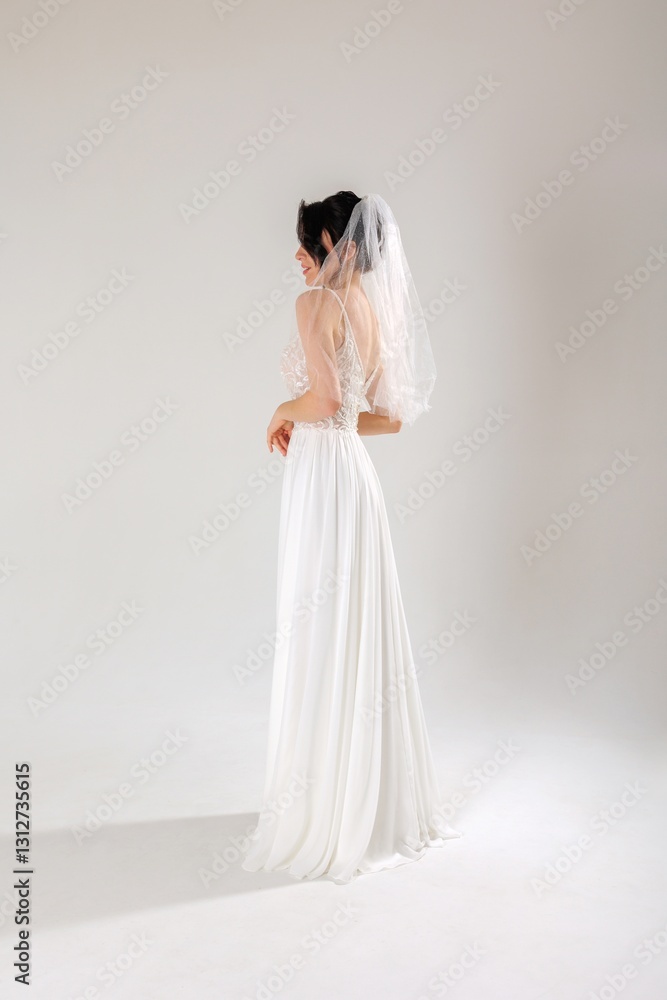 Fototapeta premium Elegant bride in white gown with veil poses gracefully in a studio setting before her wedding day