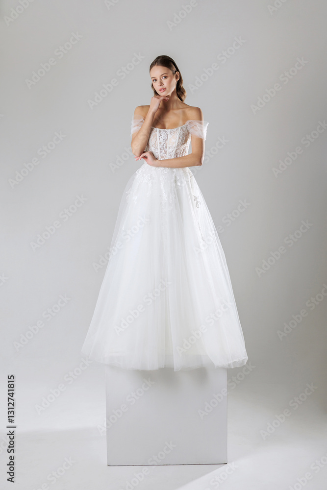 Elegant bride in a delicate white gown poses gracefully on a pedestal in a minimalist studio setting Elegant bride in a delicate white gown poses gracefully on a pedestal in a minimalist studio setting