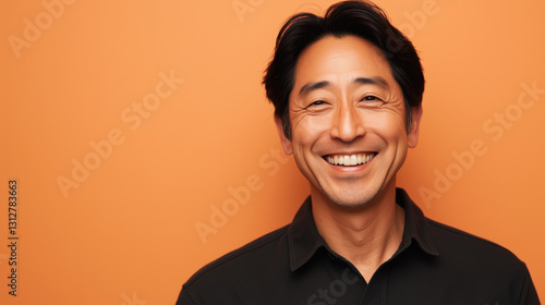 East Asian Man in His Mid-30s Smiling Warmly While Standing Against Solid Light Orange Background