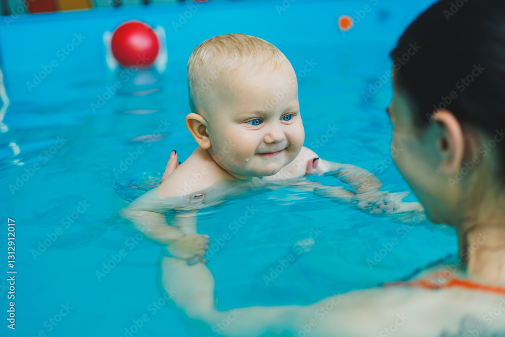 Mom and baby enjoy swimming in the pool. Baby boy learns to swim with a lifeguard.