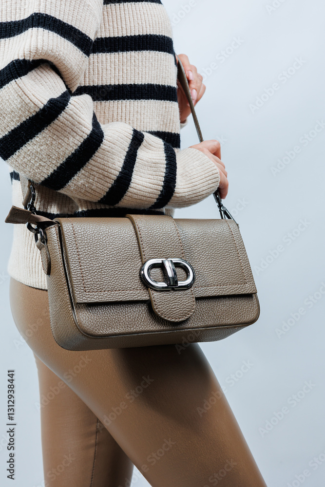 Small beige leather bag in a female hand on a white background. Shoulder bag. Woman with a beige handbag. Style, fashion, vintage and elegance.