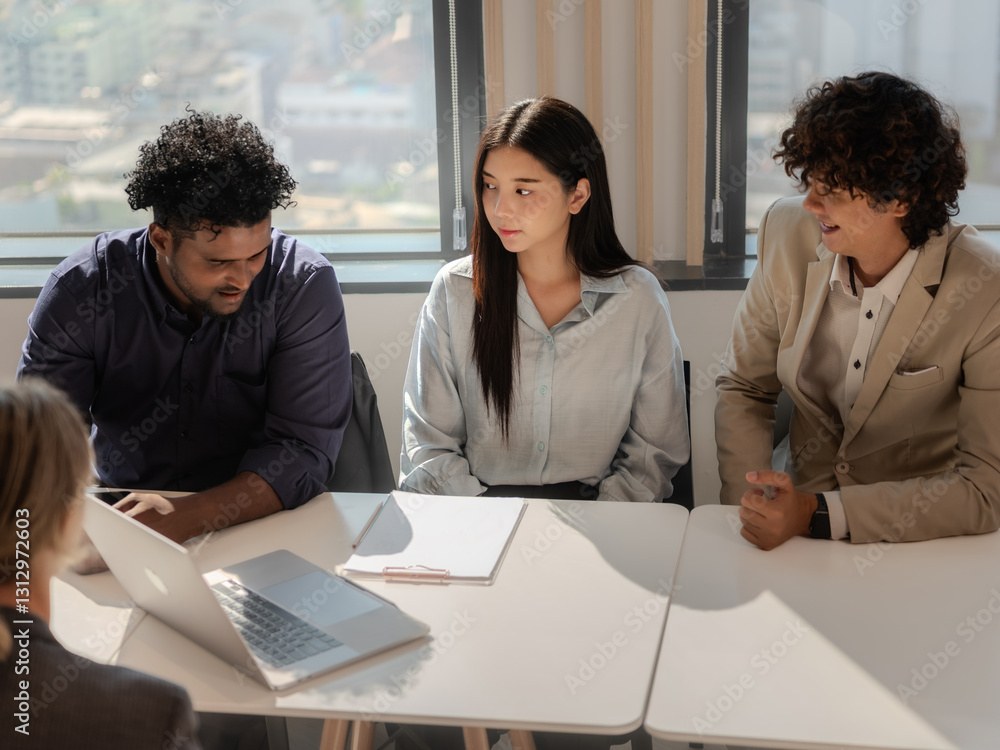 Diverse group of business professionals having a meeting, discussing strategies and ideas together in a modern office environment with technology like laptops on the table.