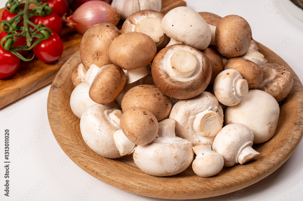 White and brown champignons mushrooms fresh uncooked on wooden plate copy space on white background White and brown champignons mushrooms fresh uncooked on wooden plate copy space on white background