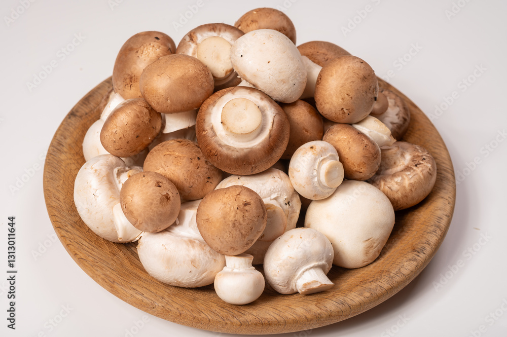 White and brown champignons mushrooms fresh uncooked on wooden plate copy space on white background White and brown champignons mushrooms fresh uncooked on wooden plate copy space on white background