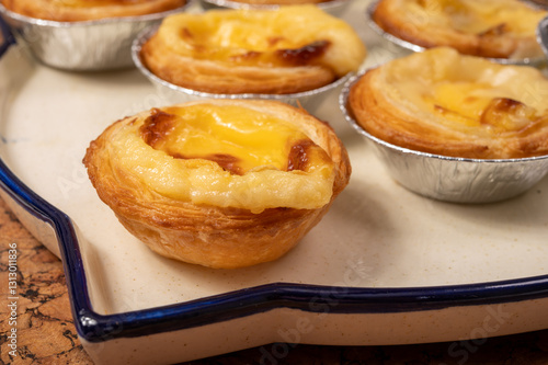 Portugal's traditional sweet dessert Pastel de nata egg custard tart pastry in cup close up on wooden background