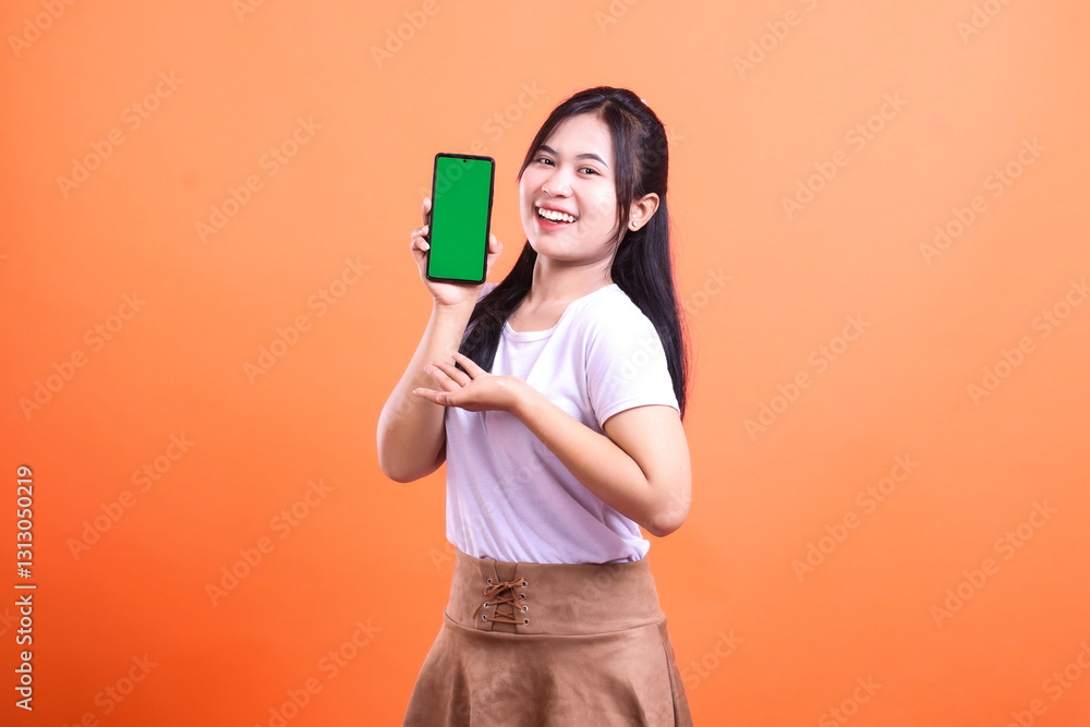 Woman presenting mobile phone with green screen on orange background in a studio Woman presenting mobile phone with green screen on orange background in a studio