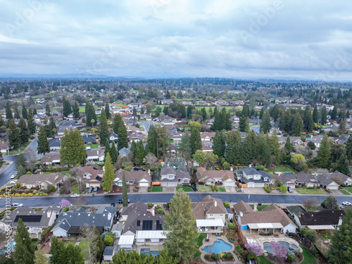 Aerial photographs over the Maidu Neighborhood in Roseville, California with green trees, streets, homes and a cloudy sky