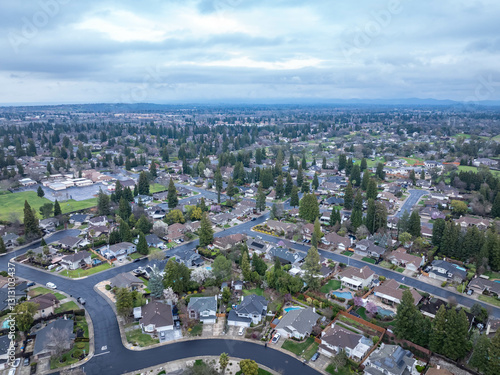 Aerial photographs over the Maidu Neighborhood in Roseville, California with green trees, streets, homes and a cloudy sky