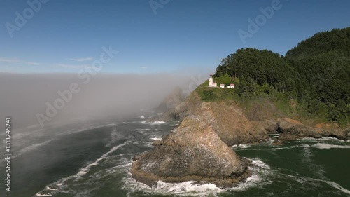 Aerial footage of Heceta Head Lighthouse on the Oregon Coast, perched atop a rugged cliff with waves crashing below. Misty ocean views and rocky seascape captured in October. photo