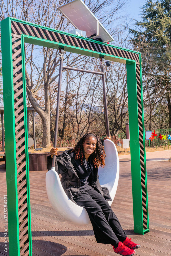 Obraz premium Young black woman enjoying a swing in a sunny park.