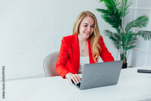 Business woman in red suit at desk with laptop in office online