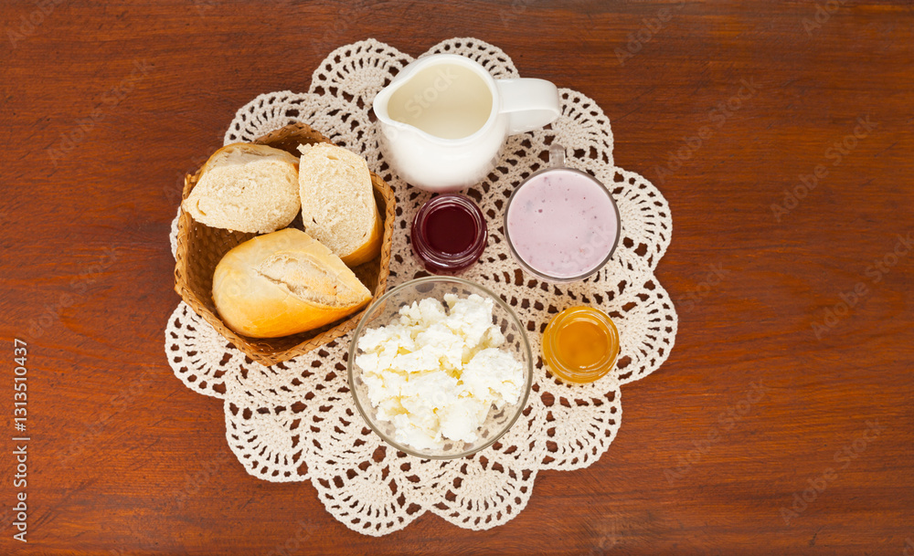 Top view of delicious country breakfast with white bread and fresh dairy products - cottage cheese, yogurt, milk on hand-knitted lace napkin on wooden table. Rustic still life. Flat lay, close-up Top view of delicious country breakfast with white bread and fresh dairy products - cottage cheese, yogurt, milk on hand-knitted lace napkin on wooden table. Rustic still life. Flat lay, close-up