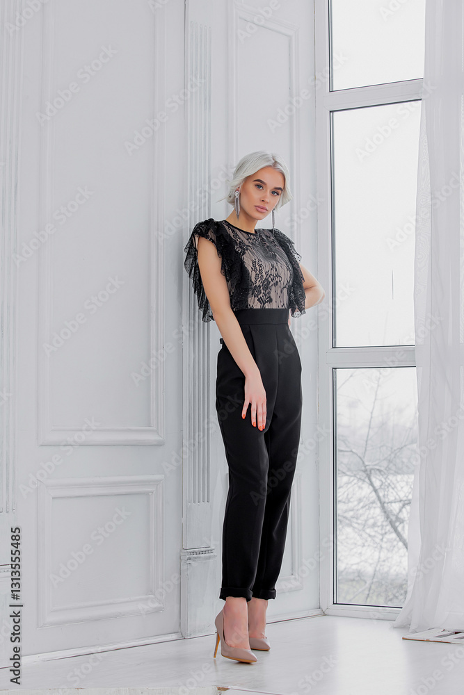 Fototapeta premium Young beautiful blonde model girl with hair and makeup in a fashionable black jumpsuit