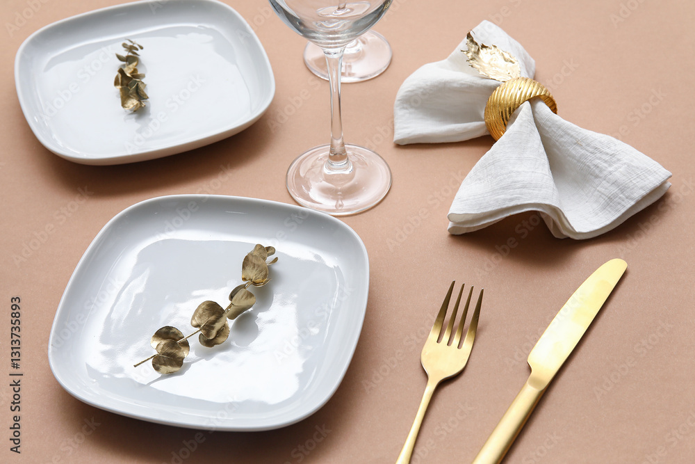 Elegant table setting with golden cutlery, leaves and napkin on beige table Elegant table setting with golden cutlery, leaves and napkin on beige table