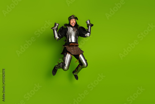 Tableau sur toile Energetic medieval knight jumping joyfully against a vibrant green background