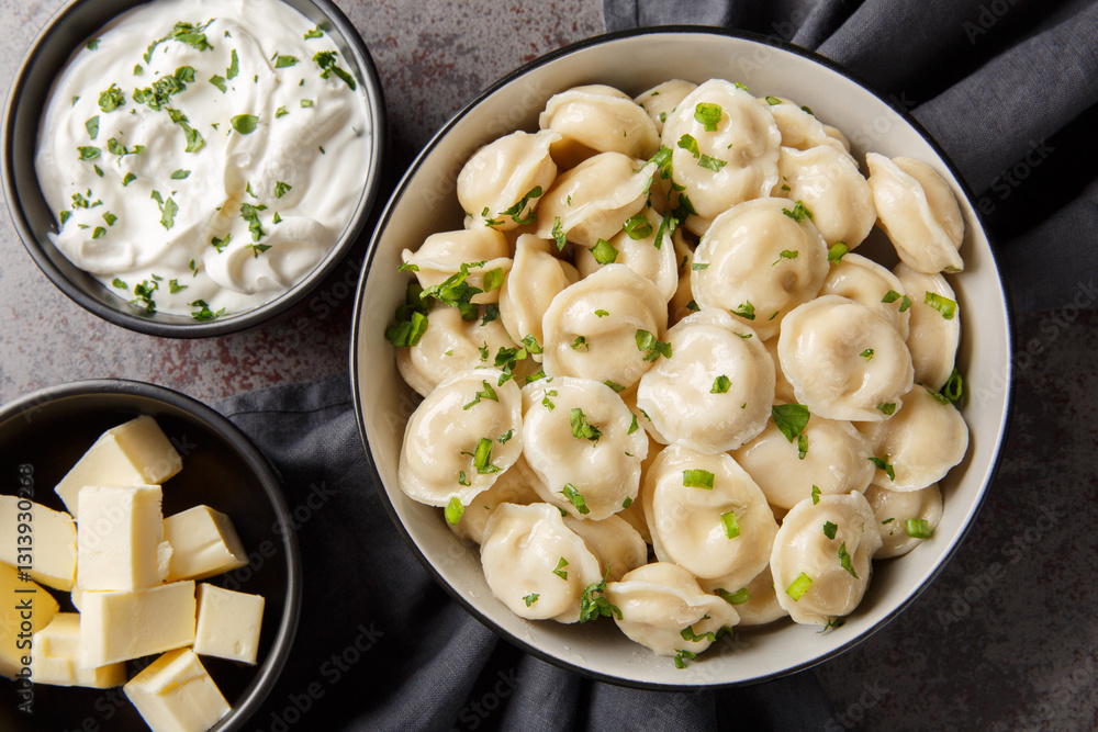 Russian cuisine dumplings in a bowl served with sour cream, butter and herbs close-up on the table. Horizontal top view from above