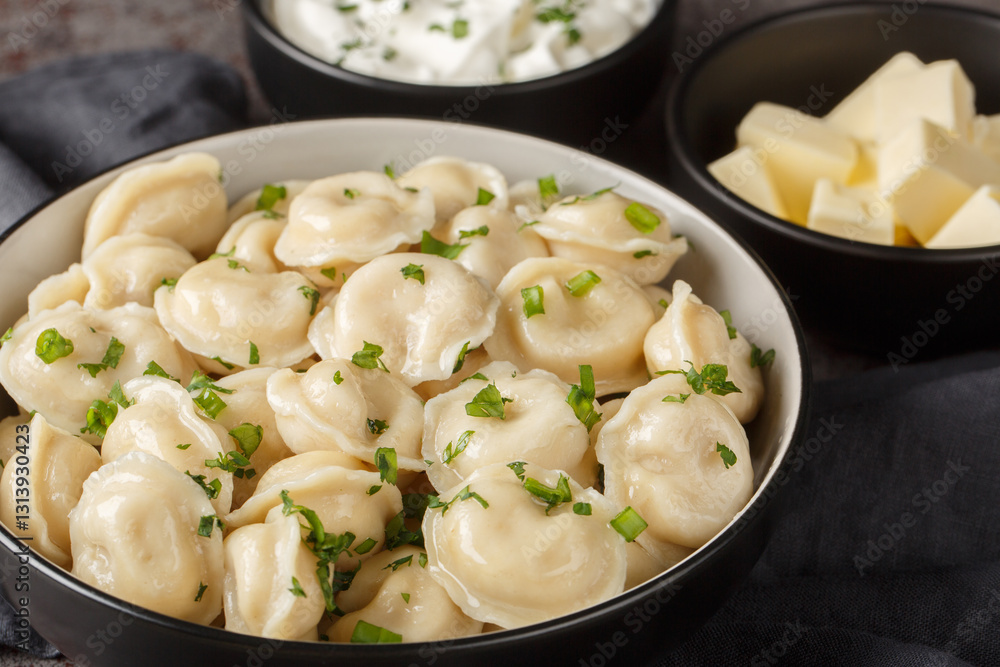 Pelmeni dumplings filled minced meat served with sour cream, butter and herbs close-up on the table. Horizontal