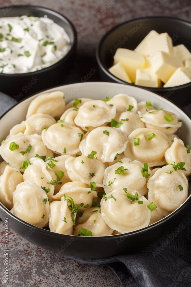 Hot boiled Russian pelmeni served with sour cream, butter and herbs close-up on the table. Vertical