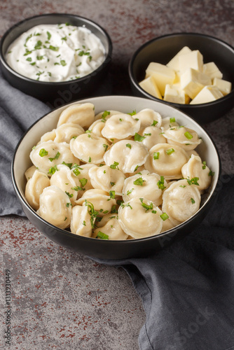 Russian cuisine dumplings in a bowl served with sour cream, butter and herbs close-up on the table. Vertical