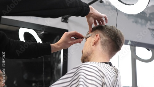 Skilled barber performing precise hair fade using straight razor, working on client's hair in contemporary grooming salon with professional tools