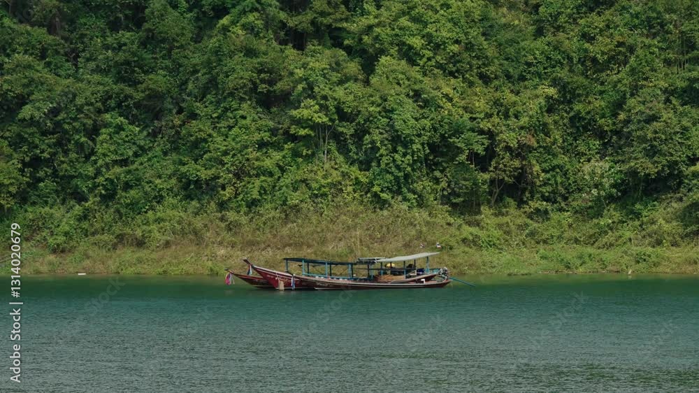 Anchored Wooden Longboat At The Shores Of Cheow Lan Lake In Khao Sok National Park, Thailand. Wide Shot Anchored Wooden Longboat At The Shores Of Cheow Lan Lake In Khao Sok National Park, Thailand. Wide Shot
