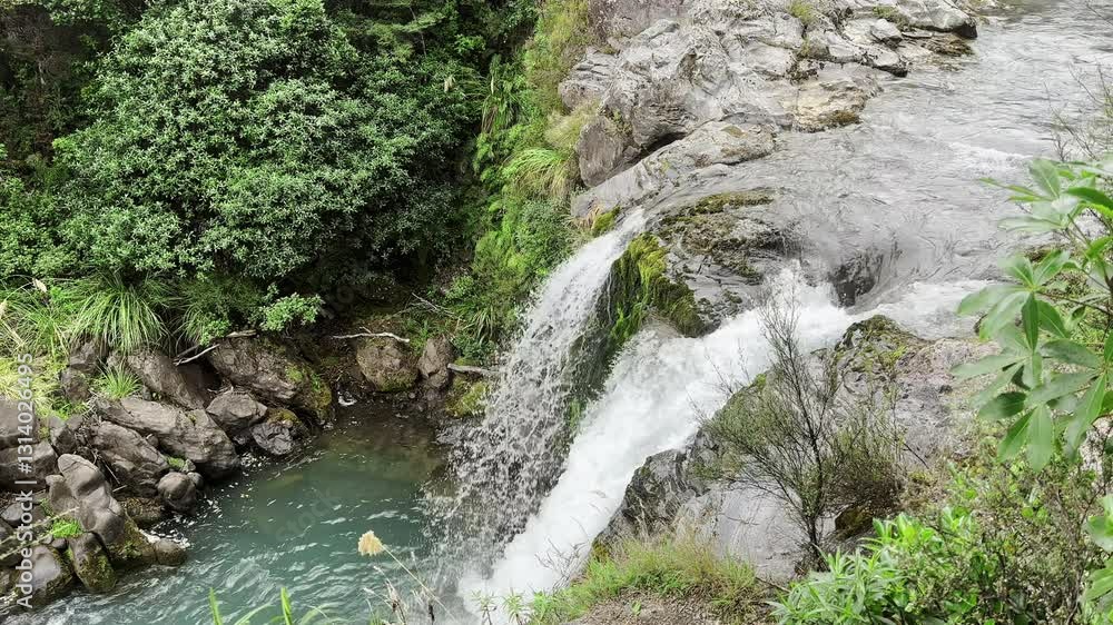 Pristine waterfall cascading over rocks in a lush green forest, creating a tranquil and scenic natural landscape Pristine waterfall cascading over rocks in a lush green forest, creating a tranquil and scenic natural landscape