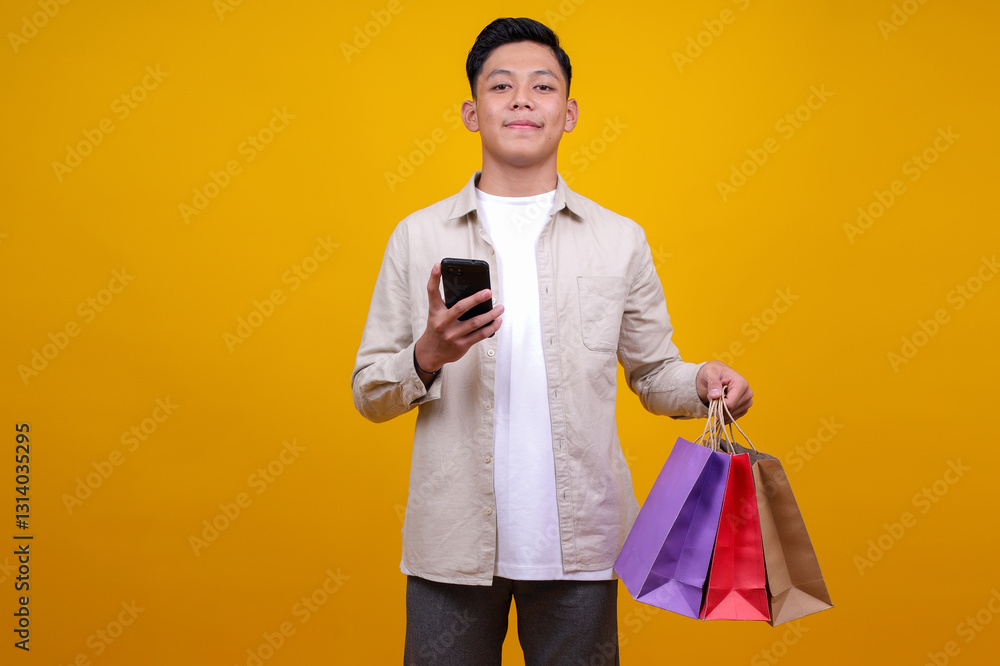 Smiling Asian Man Using Smartphone While Bring Shopping Bags Isolated on Yellow Background Smiling Asian Man Using Smartphone While Bring Shopping Bags Isolated on Yellow Background