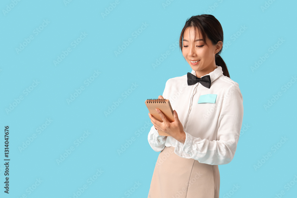 Young Asian smiling waitress with notebook on blue background Young Asian smiling waitress with notebook on blue background