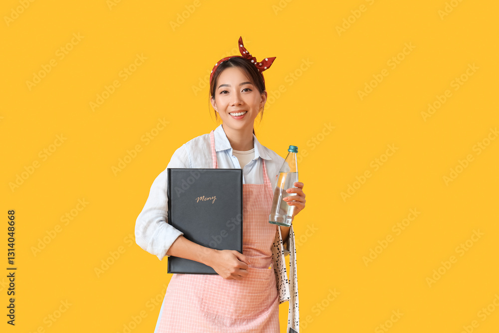 Young Asian smiling waitress with menu and bottle of water on yellow background