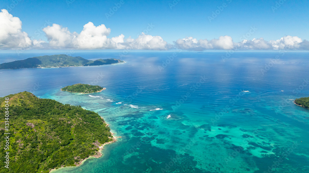 Lush green islands surrounded by clear turquoise ocean under a bright blue sky with white clouds. Seychelles, Mahe. Lush green islands surrounded by clear turquoise ocean under a bright blue sky with white clouds. Seychelles, Mahe.