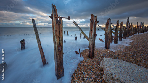Konstfotografi Rotting wooden support posts on the shingle beachwith high tide at sunset , Rye