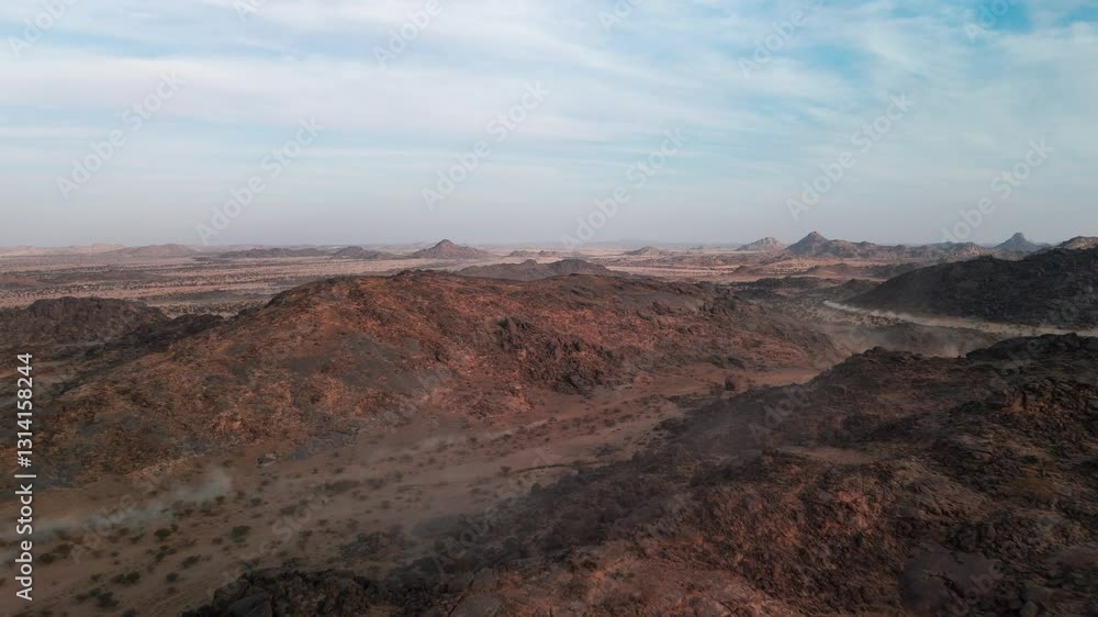Drone shot of dusty rocky desert and mountains with riding car in distance during sunset Drone shot of dusty rocky desert and mountains with riding car in distance during sunset