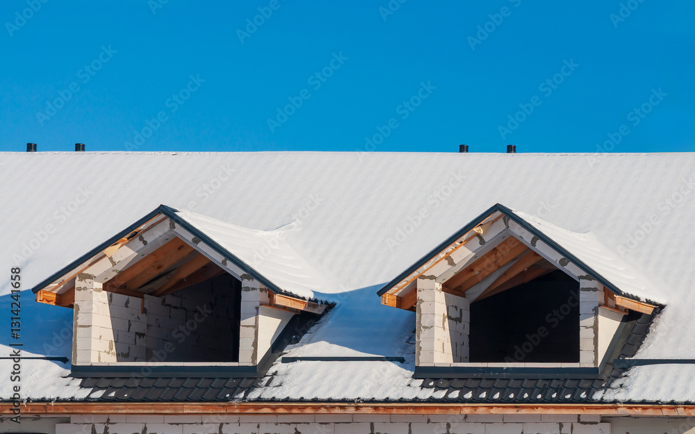 Snowy rooftop with dormer windows on an unfinished construction site against a bright blue sky. Snowy rooftop with dormer windows on an unfinished construction site against a bright blue sky.
