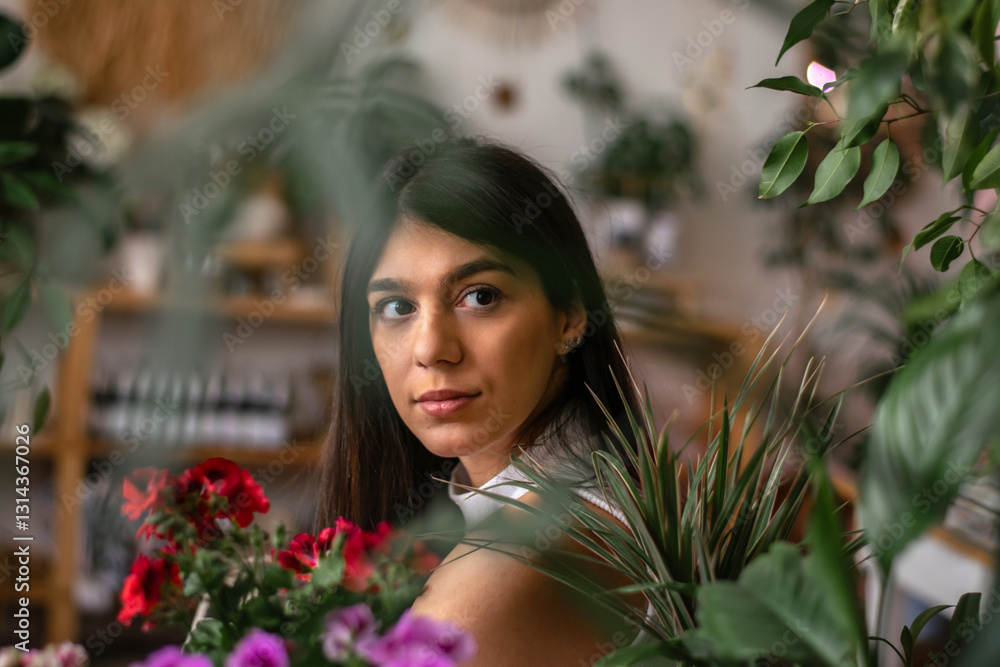 Portrait of a young happy dark-haired woman sitting in a studio with flowers and indoor plants.The spring concept,home gardening. Portrait of a young happy dark-haired woman sitting in a studio with flowers and indoor plants.The spring concept,home gardening.