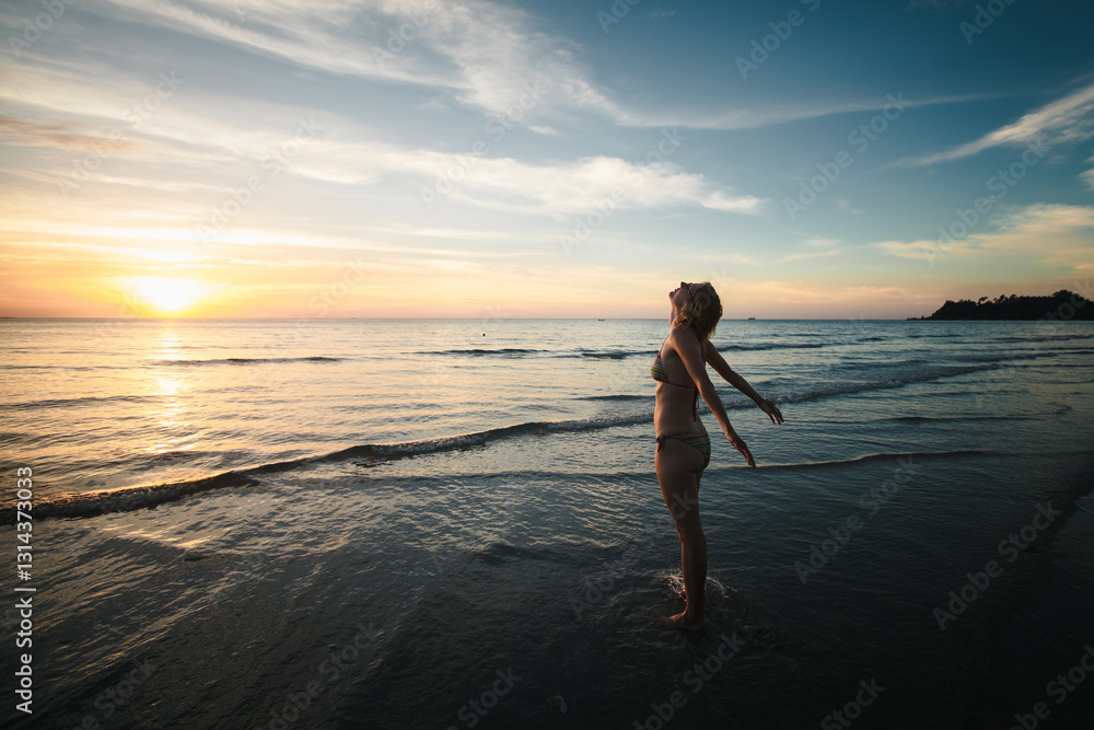 A woman in a swimsuit stands on the seashore, greeting the rising sun, surrounded by the serene beauty of the early morning.