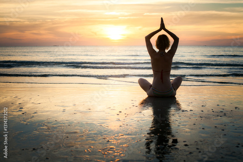 Obraz na płótnie The silhouette of a woman meditating at the water's edge during a serene sea sunset, radiating peace and tranquility. w salonie