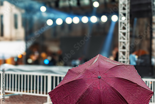 a person holding a maroon color umbrella in the rain against covered outdoor stage concert music performance rainy day