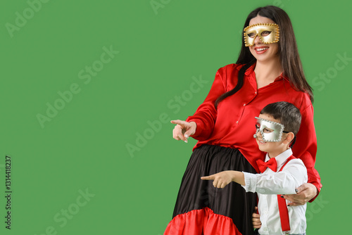 Mother and son in costumes and carnival masks pointing at something on green background photo