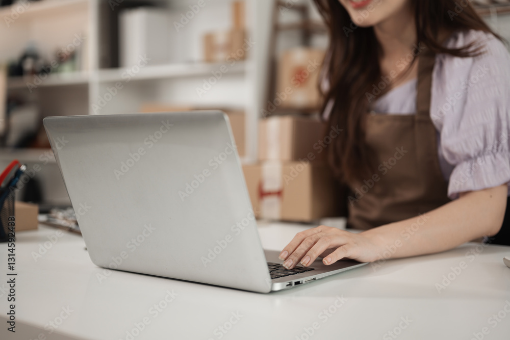 A close-up of a small business owner in an apron works on her laptop, managing orders and logistics A close-up of a small business owner in an apron works on her laptop, managing orders and logistics