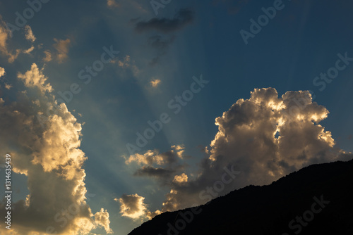 Obraz na płótnie luce calda del sole al tramonto che illumina le nuvole ed il cielo di arancione da dietro un'alta catena montuosa, in estate w salonie