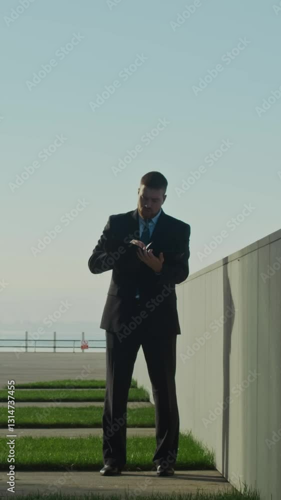 Vertical full shot of young male CEO looking through his paper documents outside in business center Vertical full shot of young male CEO looking through his paper documents outside in business center