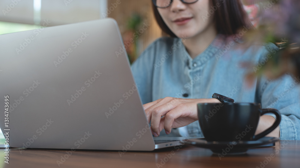 Fototapeta premium Young asian business woman working on laptop computer at coffee shop. Female freelancer online working on laptop with digital tablet on wooden table at cafe, online job, remote work