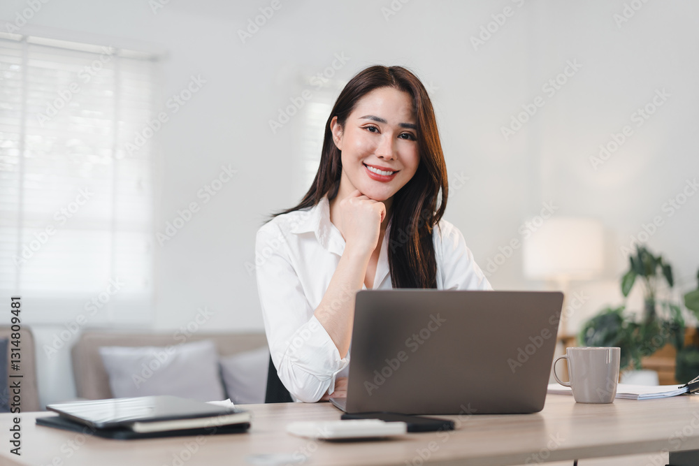 Confident Asian Businesswoman in White Shirt Working on Laptop at Modern Home Office Desk. Confident Asian Businesswoman in White Shirt Working on Laptop at Modern Home Office Desk.