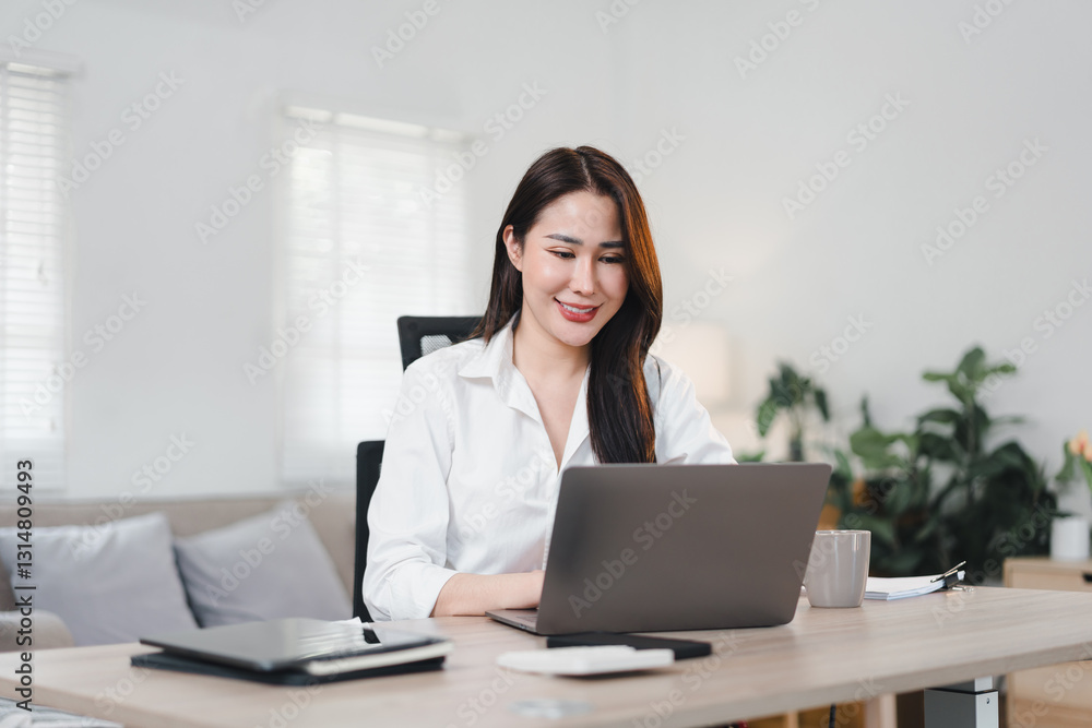 Asian Businesswoman in White Shirt Working on Laptop at Desk in Bright, Modern Home Office. Asian Businesswoman in White Shirt Working on Laptop at Desk in Bright, Modern Home Office.