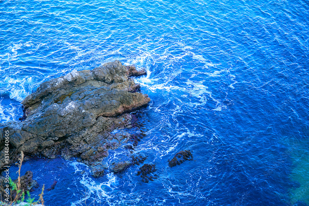 Obraz premium A view from above of the seashore and the surf. The waves break on the rocky shore. Sea view from above