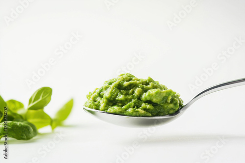 A spoonful of creamy, green avocado mash with fresh basil leaves in a minimalist setting.