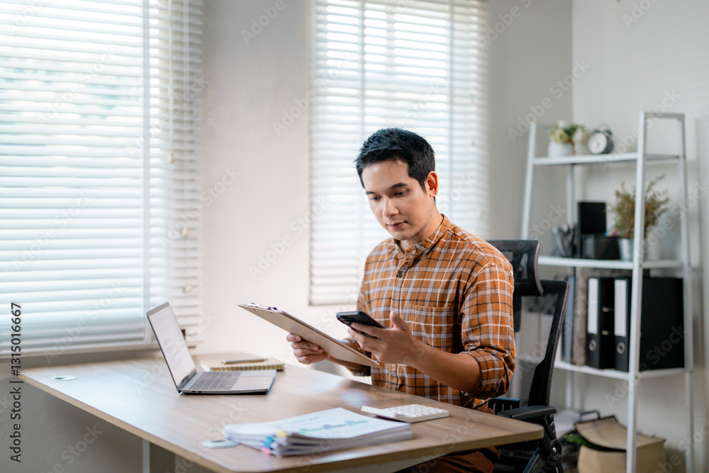 Asian entrepreneur sitting at desk comparing data from mobile phone and documents, working remotely in home office Asian entrepreneur sitting at desk comparing data from mobile phone and documents, working remotely in home office