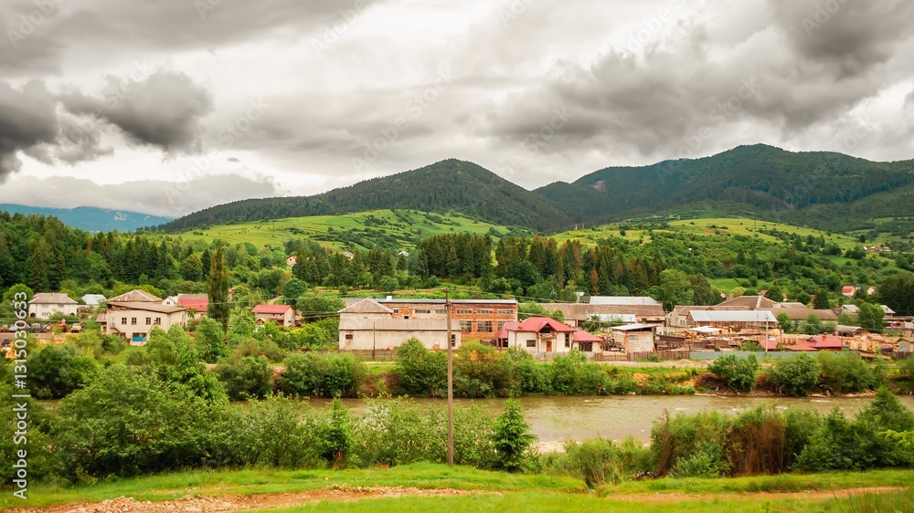 Picturesque village nestled in green hills by a river under a cloudy sky offers a tranquil landscape.