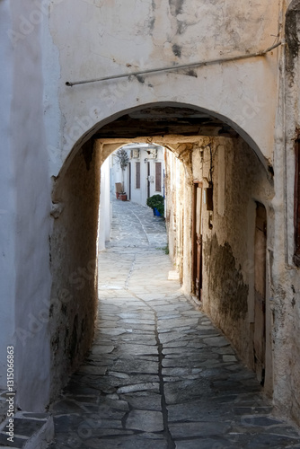 Narrow alley with tunnel and with whitewashed walls and stone pavement leading to a courtyard in the Greek Islands, Greece